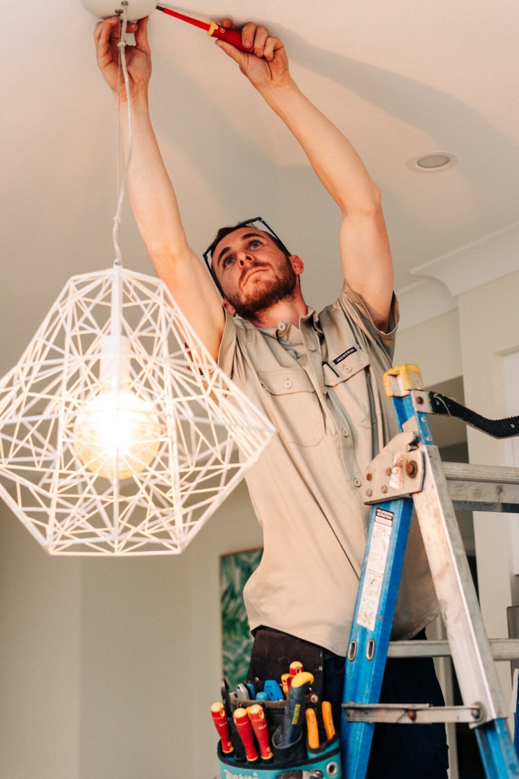 A man installing a light fixture on a ladder.